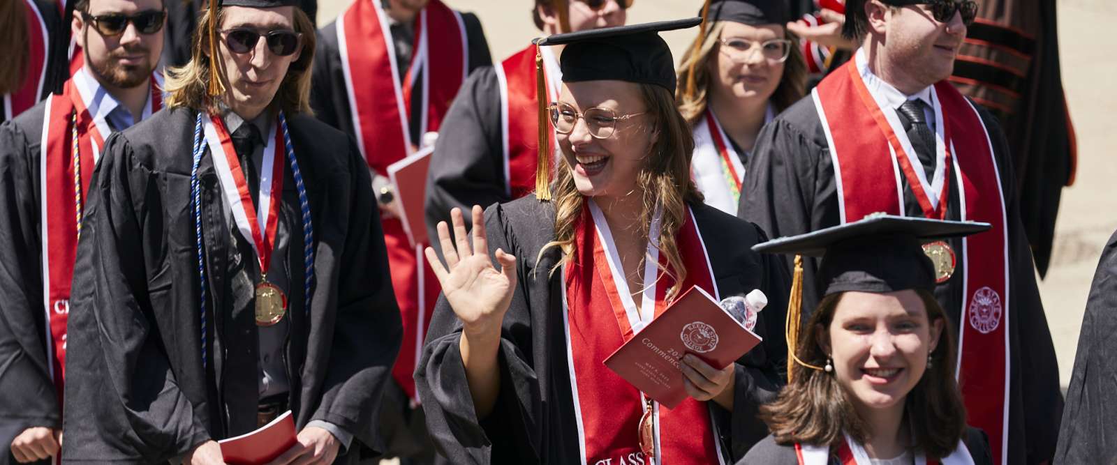 A graduate waves to her family and friends during the procession to Fiske Quad